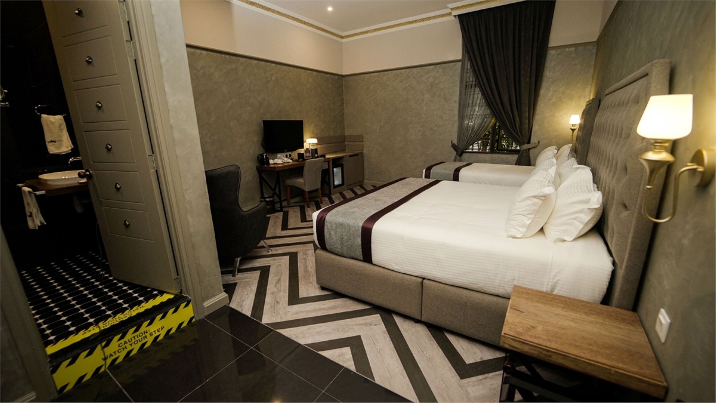 Habitación de hotel con una cama grande, un escritorio, una silla, un televisor y un baño con perchero.