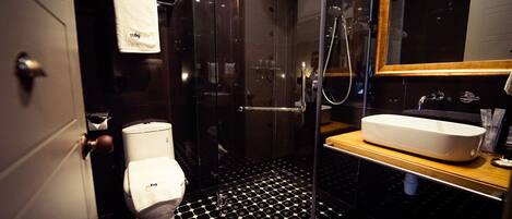 A modern bathroom with a black and white hexagonal tile floor, a white toilet, a glass-enclosed shower, and a wooden vanity with a white sink.