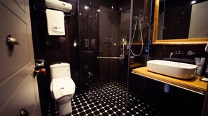 A modern bathroom with a black and white hexagonal tile floor, a white toilet, a glass-enclosed shower, and a wooden vanity with a white sink. - 1969 Ipoh Garden (Ipoh)