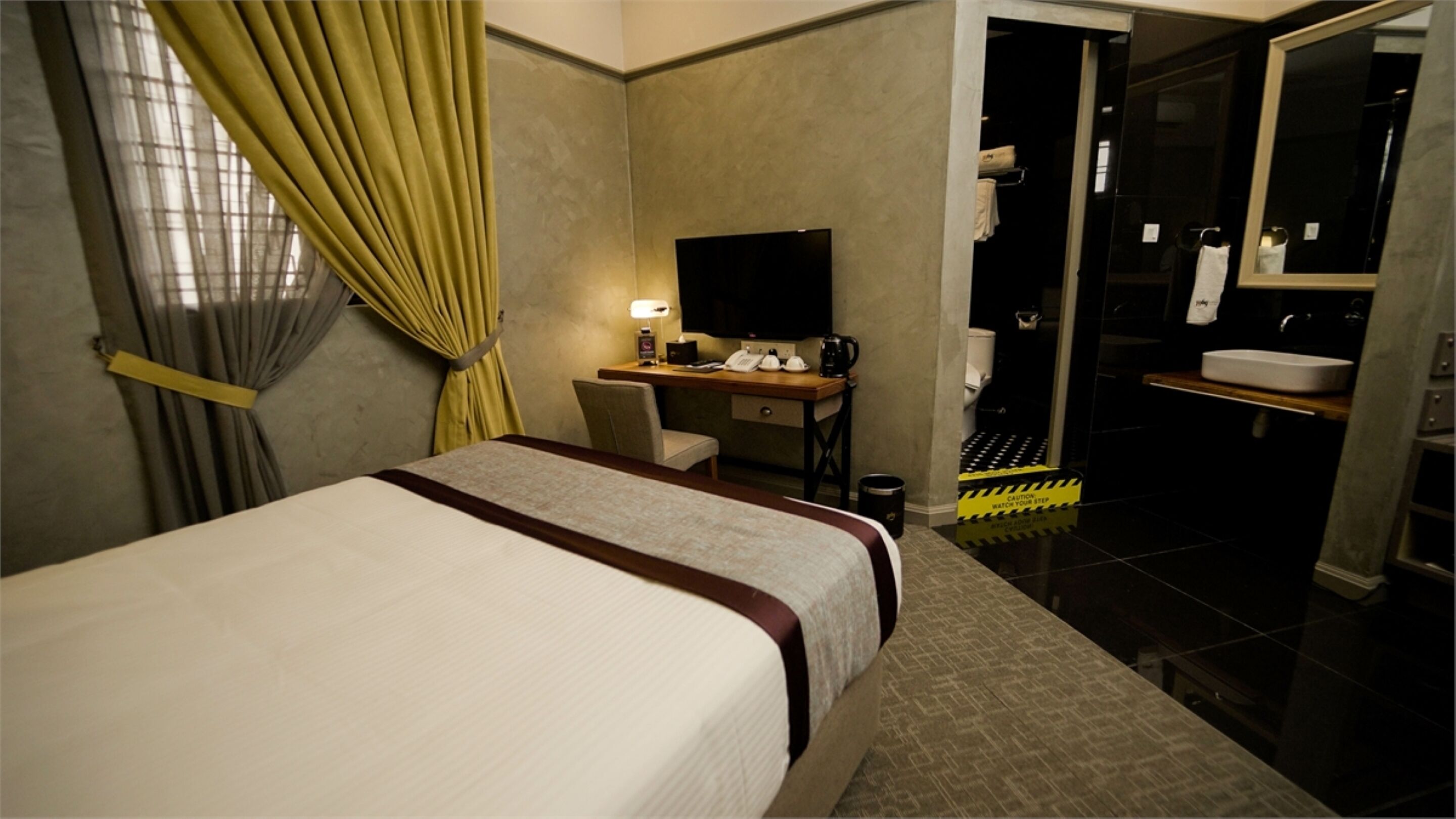 A hotel room with a bed, desk, and a bathroom with a shower and sink.
