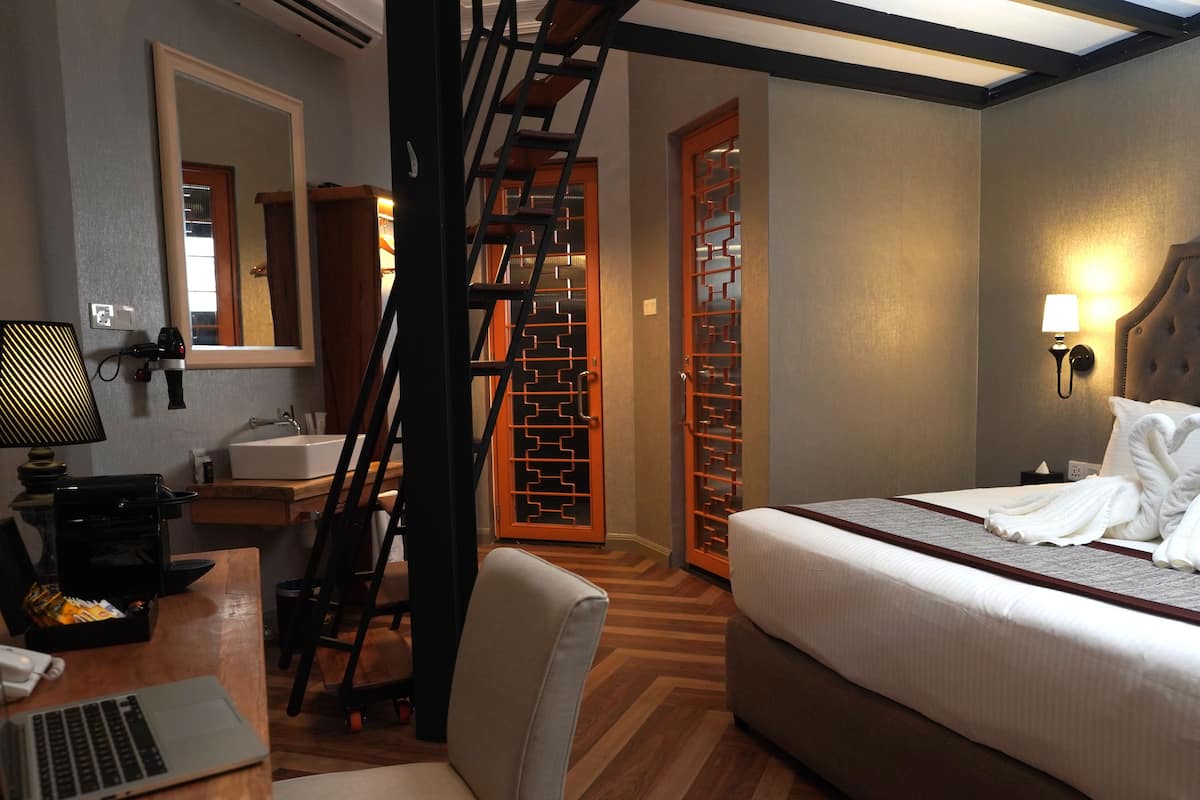 Ein Hotelzimmer mit einem Bett, einem Schreibtisch mit Laptop, einem Stuhl, einem Spiegel und einer Treppe.