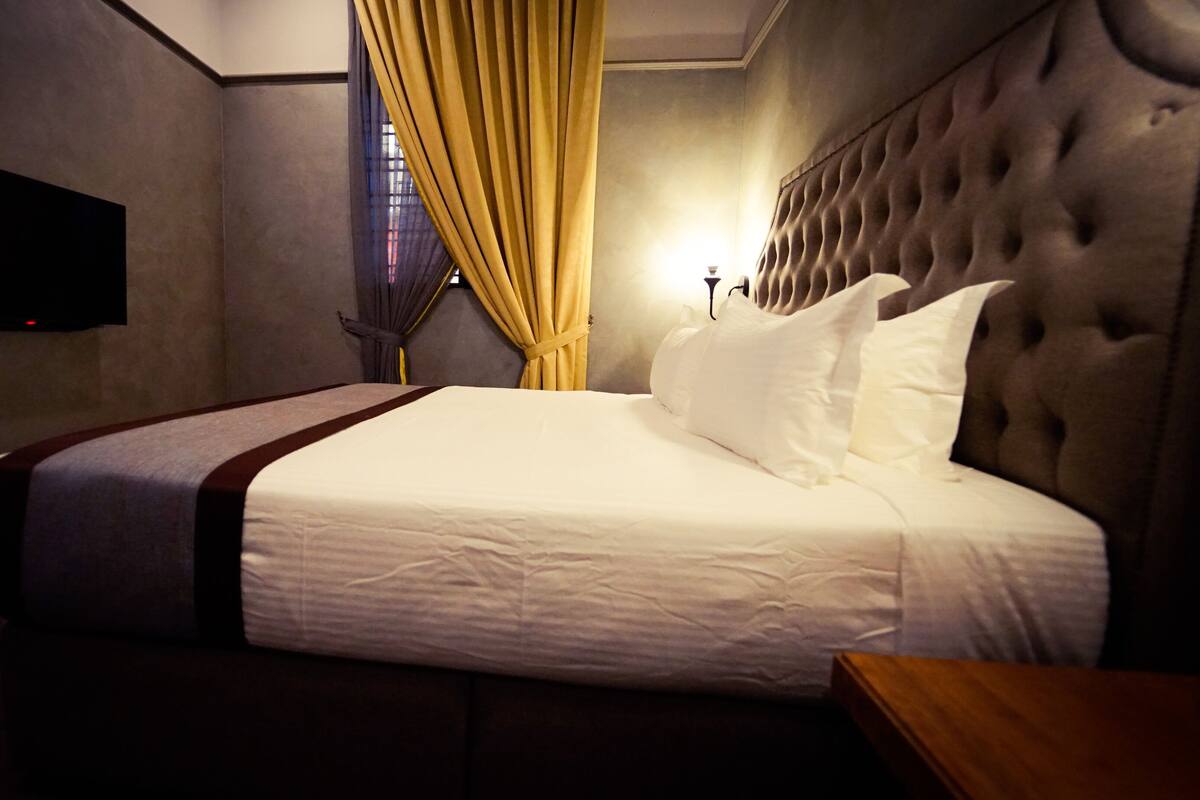 Ein Hotelzimmer mit einem großen Bett, einem an der Wand befestigten Flachbildfernseher und einem Fenster mit Vorhängen.