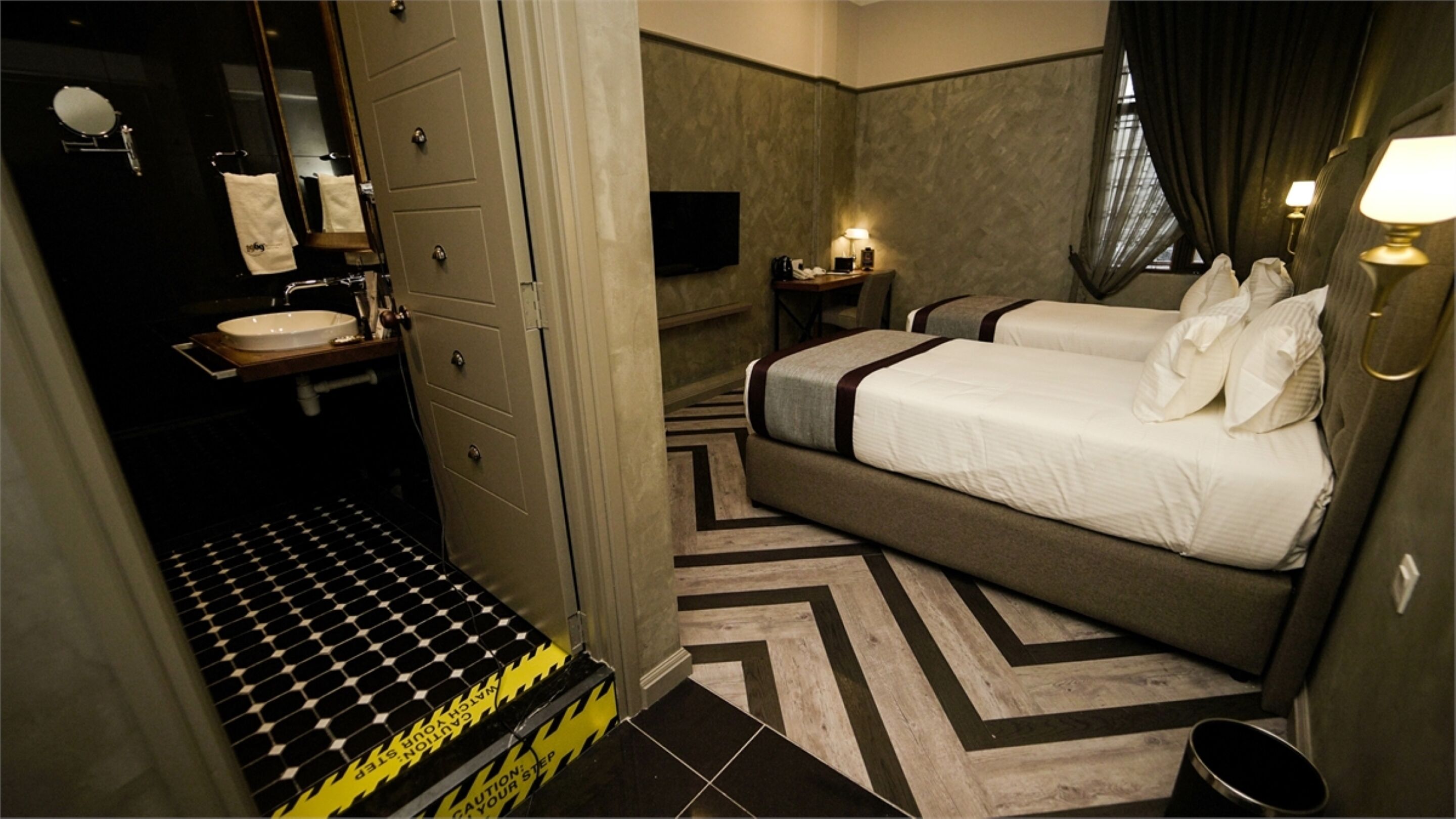 A hotel room with a bed, bedside table, and a bathroom with a sink and mirror.
