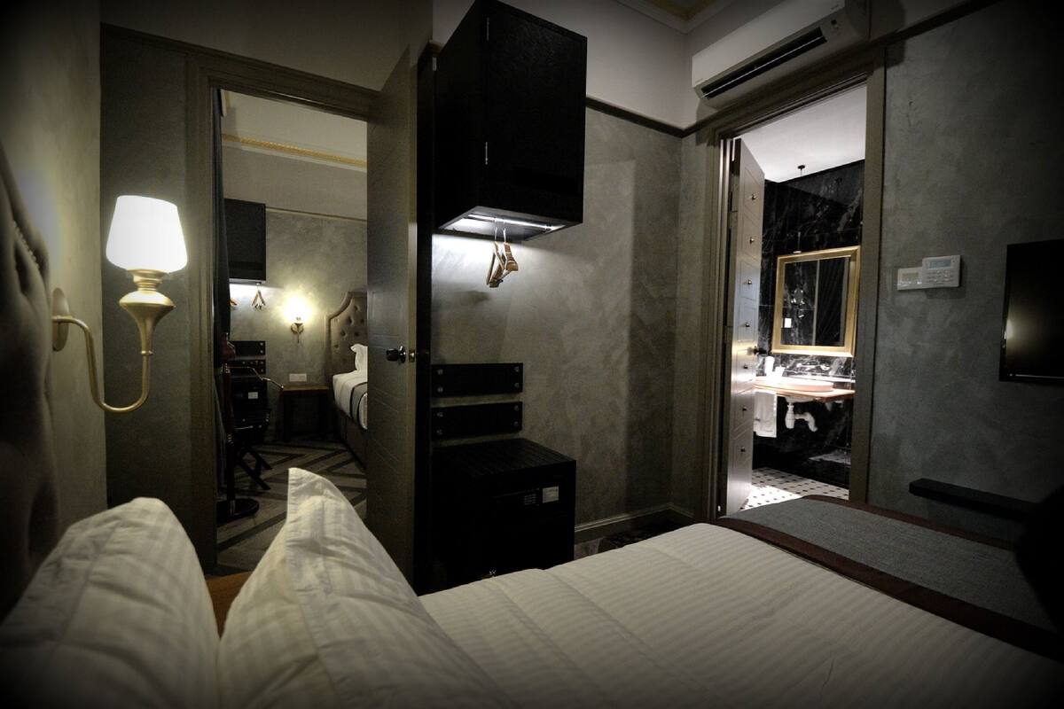Ein Hotelzimmer mit Bett, Schreibtisch, Spiegel und einem durchgehenden Türspalte sichtbaren Badezimmer.