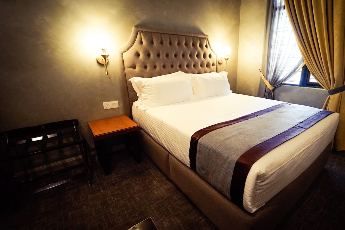 Ein Hotelzimmer mit einem großen Bett, einem Nachttisch aus Holz, einer Wandlampe und einem Fenster mit Vorhängen.