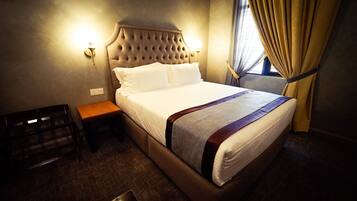 A hotel room with a large bed, a wooden nightstand, a wall-mounted lamp, and a window with curtains.