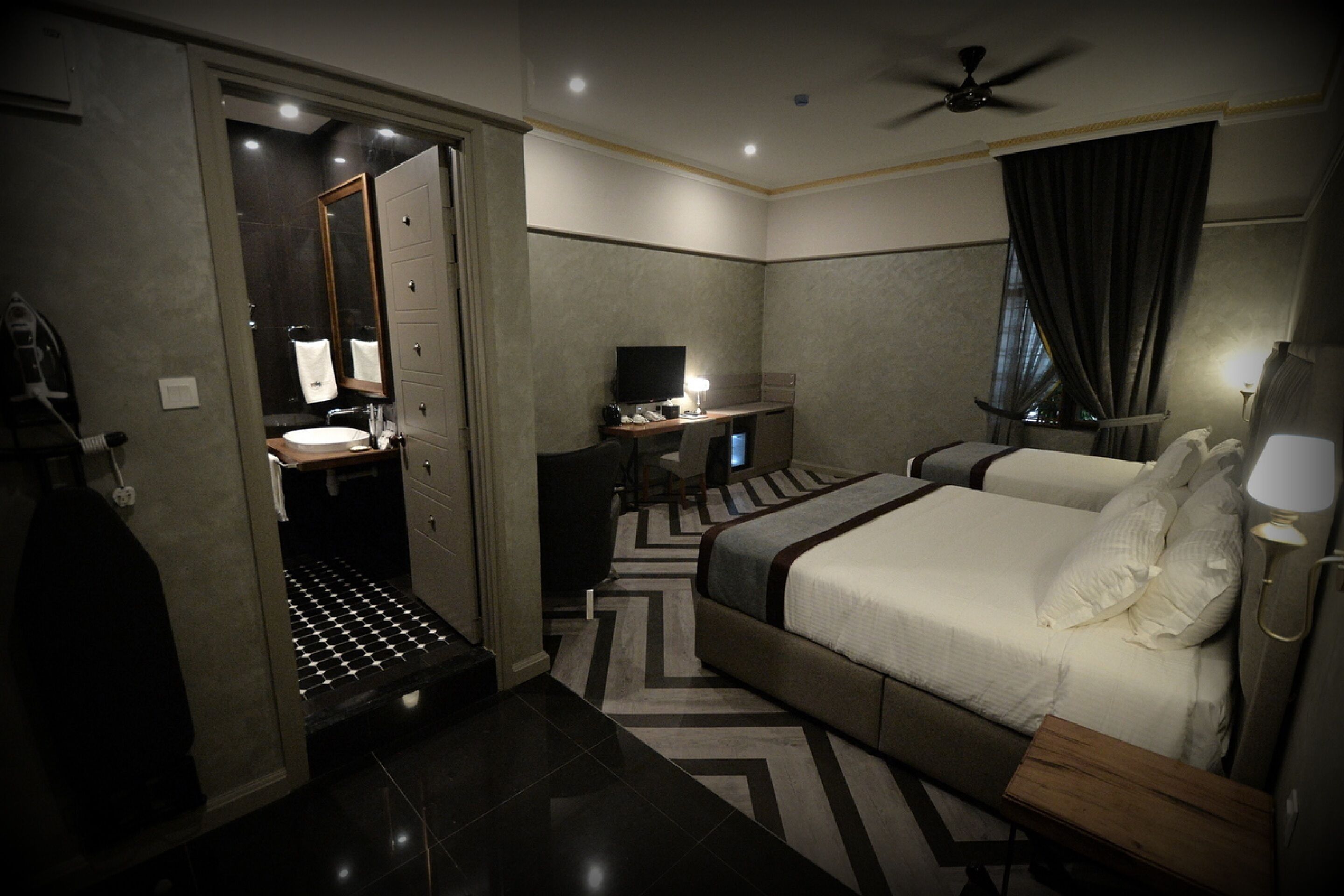 A hotel room with a bed, a desk with a computer, a mirror, and a bathroom with a sink and toilet.