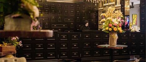 A hotel reception area with a registration desk, a chandelier, and a floral arrangement on a small table.