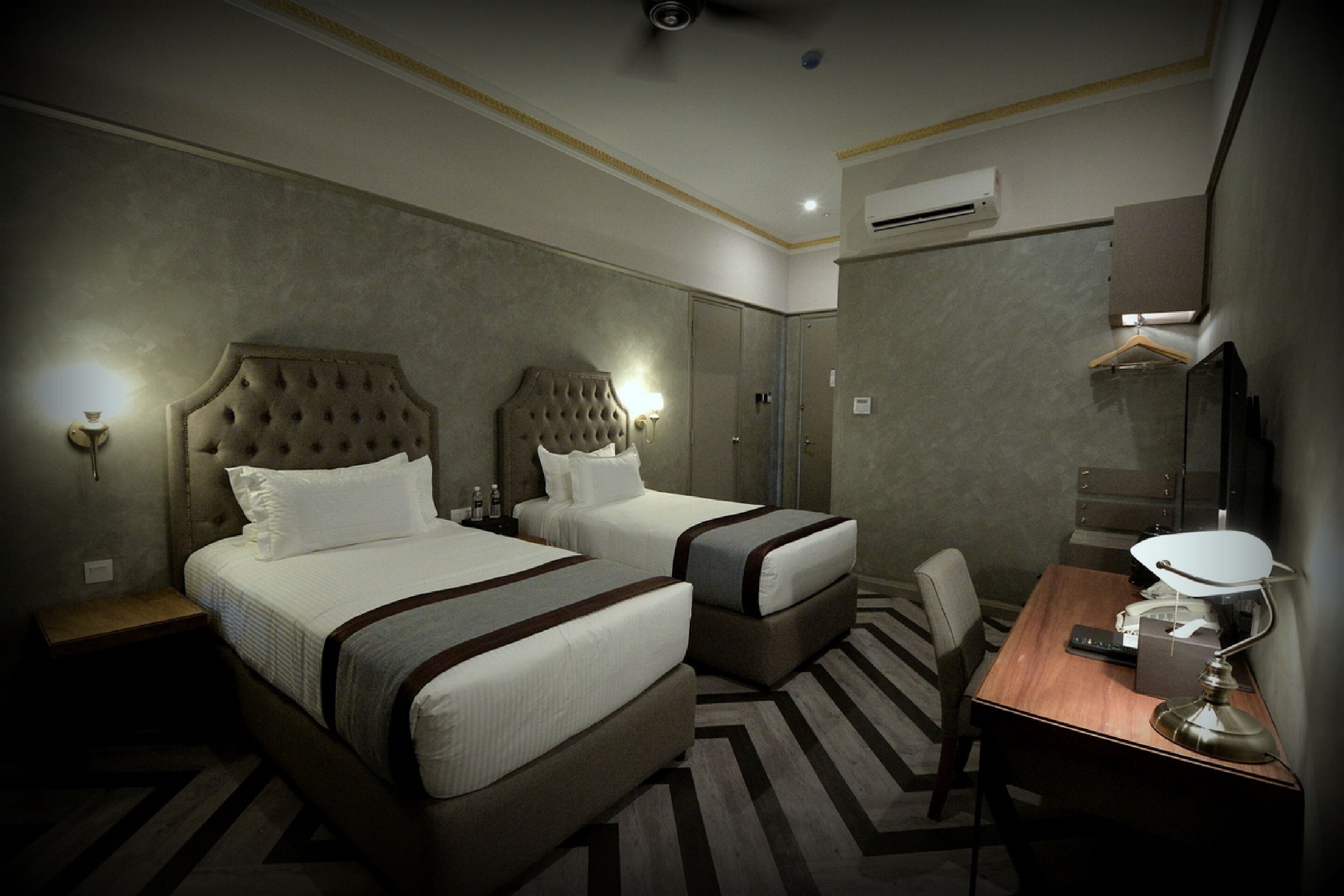 A hotel room with two beds, a desk, a chair, and an air conditioning unit.