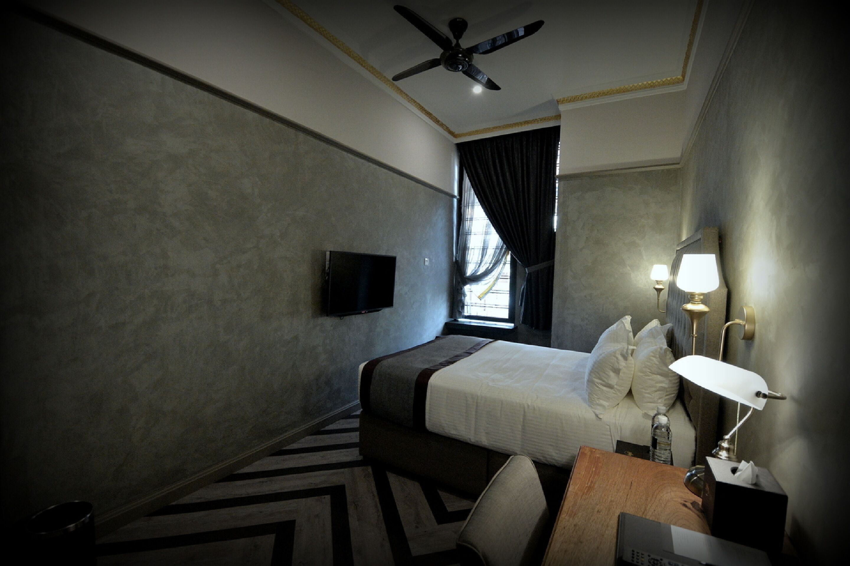 Une chambre d’hôtel équipée d’un lit, d’une télévision, d’un bureau avec une lampe et d’un ventilateur de plafond.