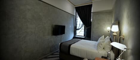 Une chambre d’hôtel équipée d’un lit, d’une télévision, d’un bureau avec une lampe et d’un ventilateur de plafond.