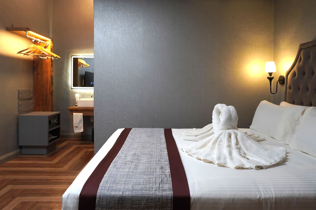 Ein Hotelzimmer mit einem großen Bett, einem Flachbildfernseher, Holzboden und einem Spiegel.