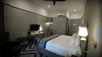 A hotel room with a bed, a desk with a computer, a chair, a TV, and a ceiling fan.