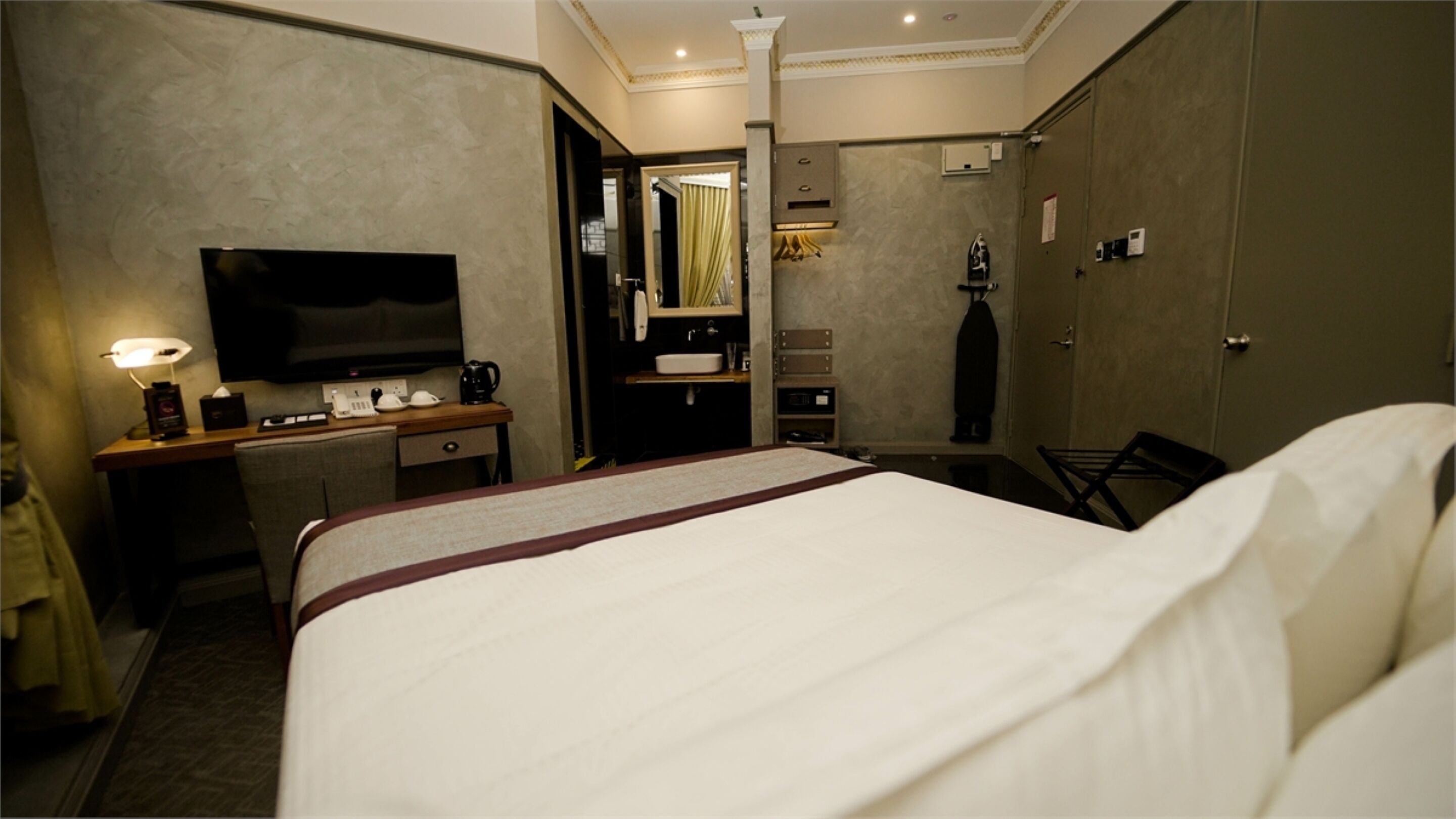 Une chambre d’hôtel avec un grand lit, un bureau avec une télévision, un miroir et une salle de bain équipée d’un lavabo et d’une douche.