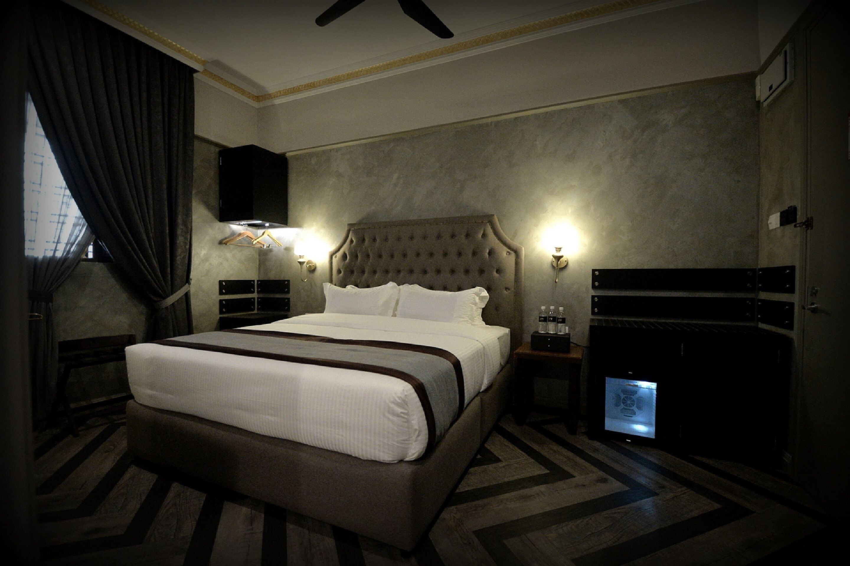 Ein Hotelzimmer mit einem großen Bett, einem Fernseher, einer Minibar und einer Schreibtischlampe.