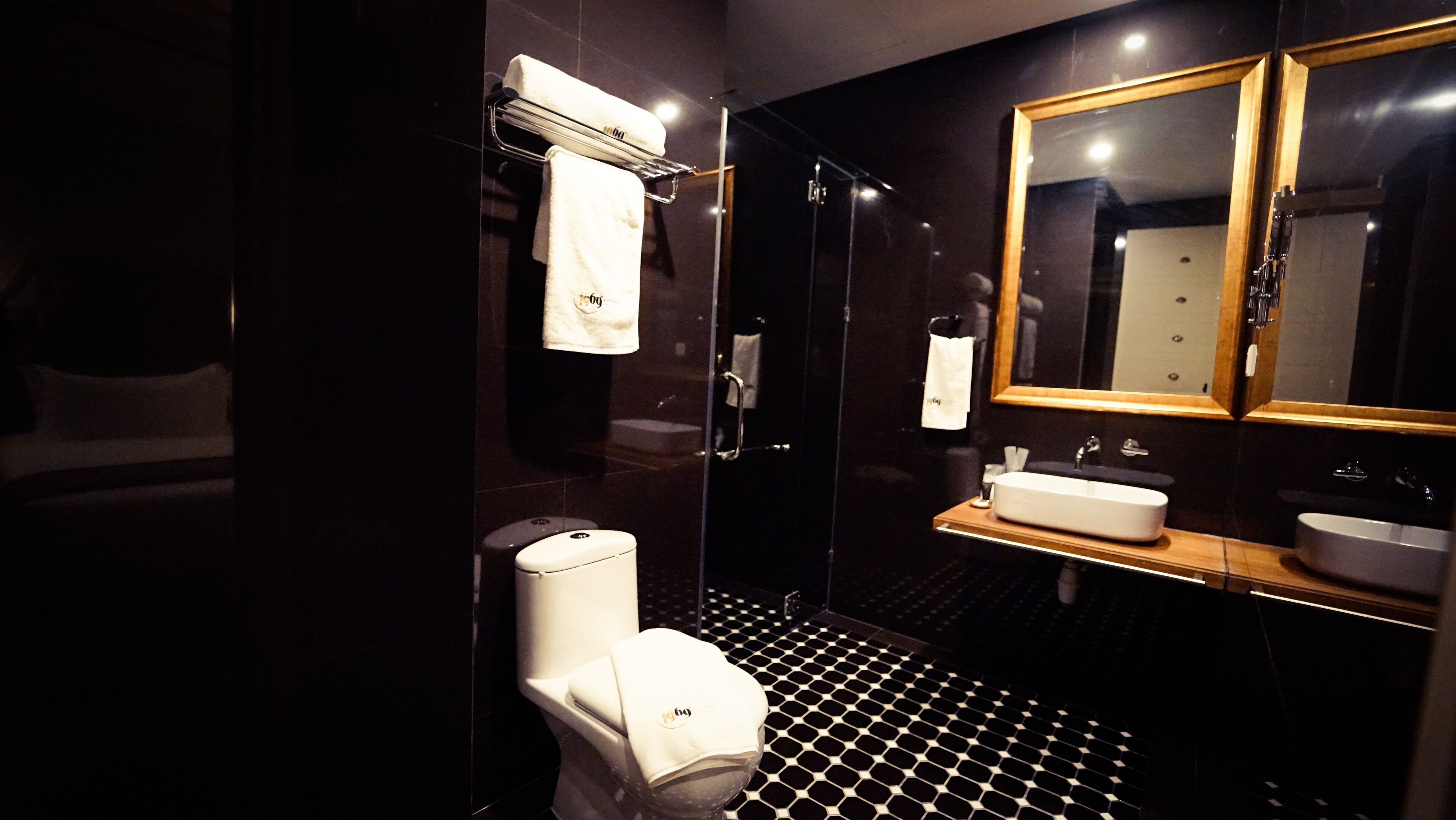 A modern bathroom with a black and white tiled floor, a white toilet, a sink with a wooden countertop, and a mirror with a wooden frame.
