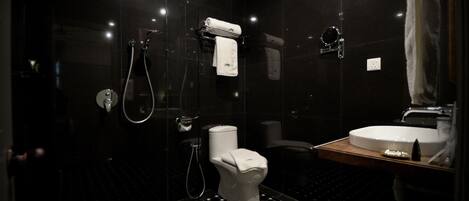 Une salle de bain moderne avec un carrelage noir et blanc à motifs géométriques, des toilettes blanches, un lavabo et une douche séparée par une paroi en verre.