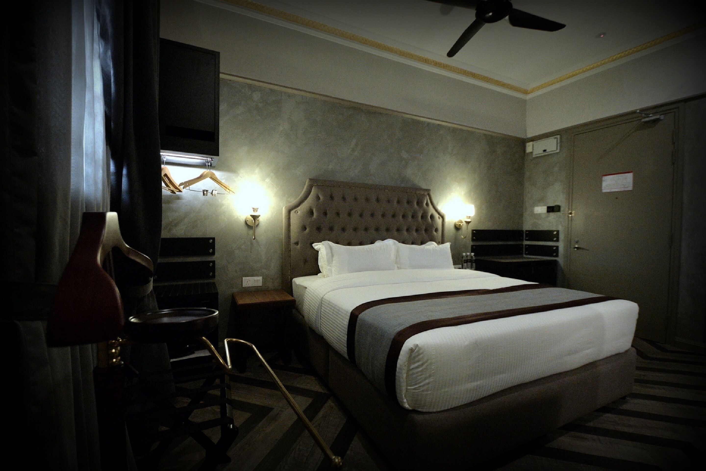 Une chambre d’hôtel avec un grand lit, un ventilateur de plafond, un téléviseur fixé au mur et une table de chevet avec une lampe.