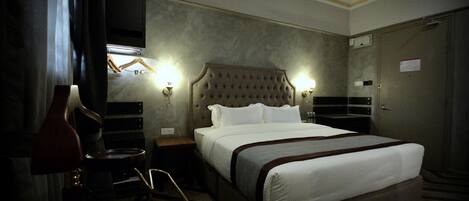 A hotel room with a large bed, a ceiling fan, a TV mounted on the wall, and a bedside table with a lamp.