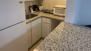 A compact kitchen with white cabinets, a granite countertop, a refrigerator, a coffee maker, a toaster, and a microwave. - Miami Airport Apartment Inn (Miami)