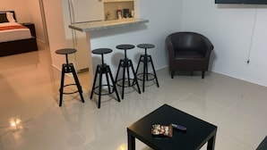 A compact living space with a kitchenette, a dining area with stools, a sofa, and a TV mounted on the wall. - Miami Airport Apartment Inn (Miami)