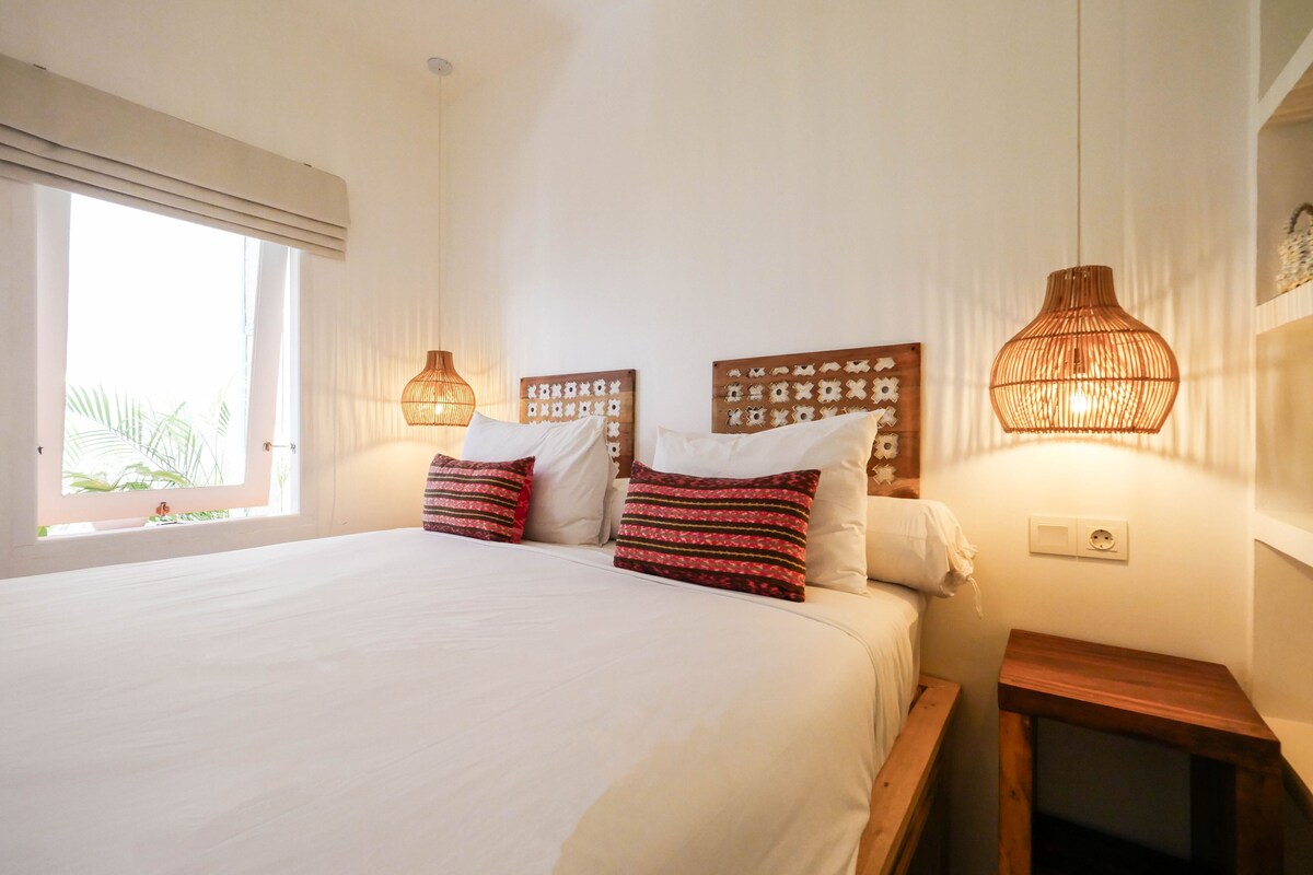 A bedroom with a large bed, two bedside lamps, and a window with curtains.