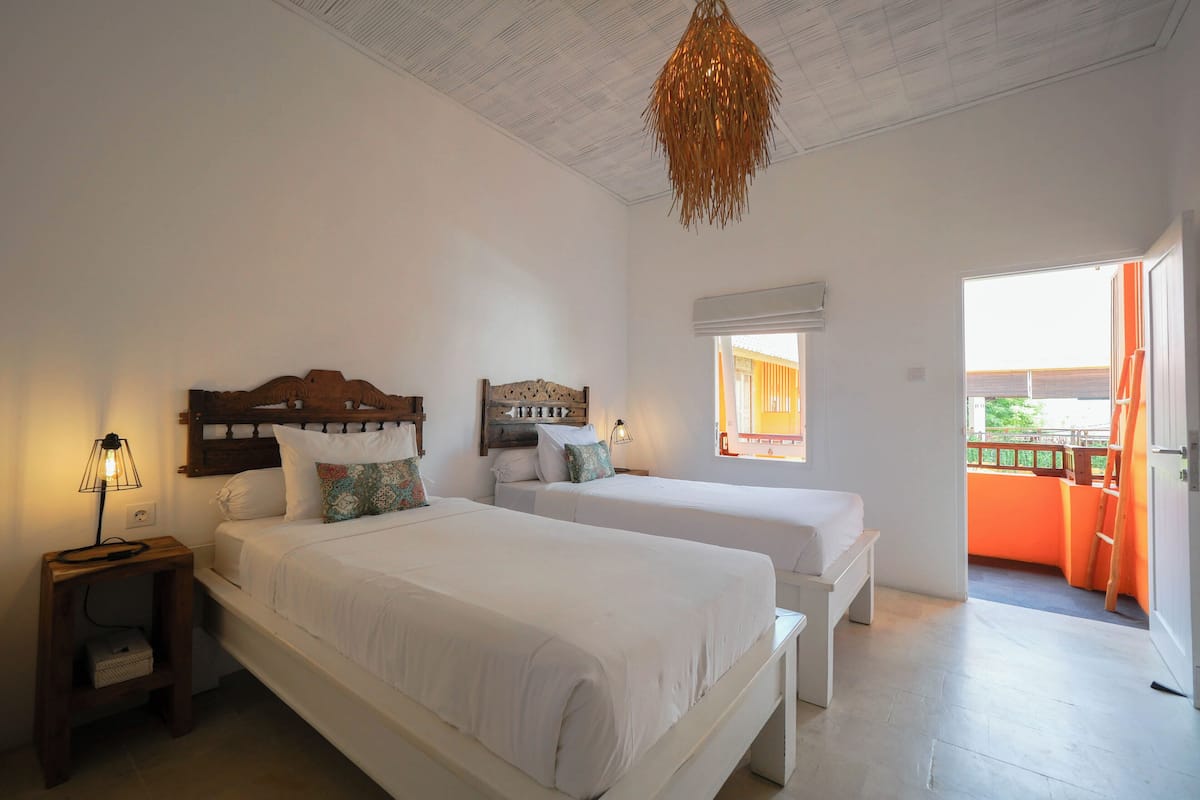 A bedroom with two beds, a wooden headboard, a nightstand, a lamp, and a view of the outside balcony.