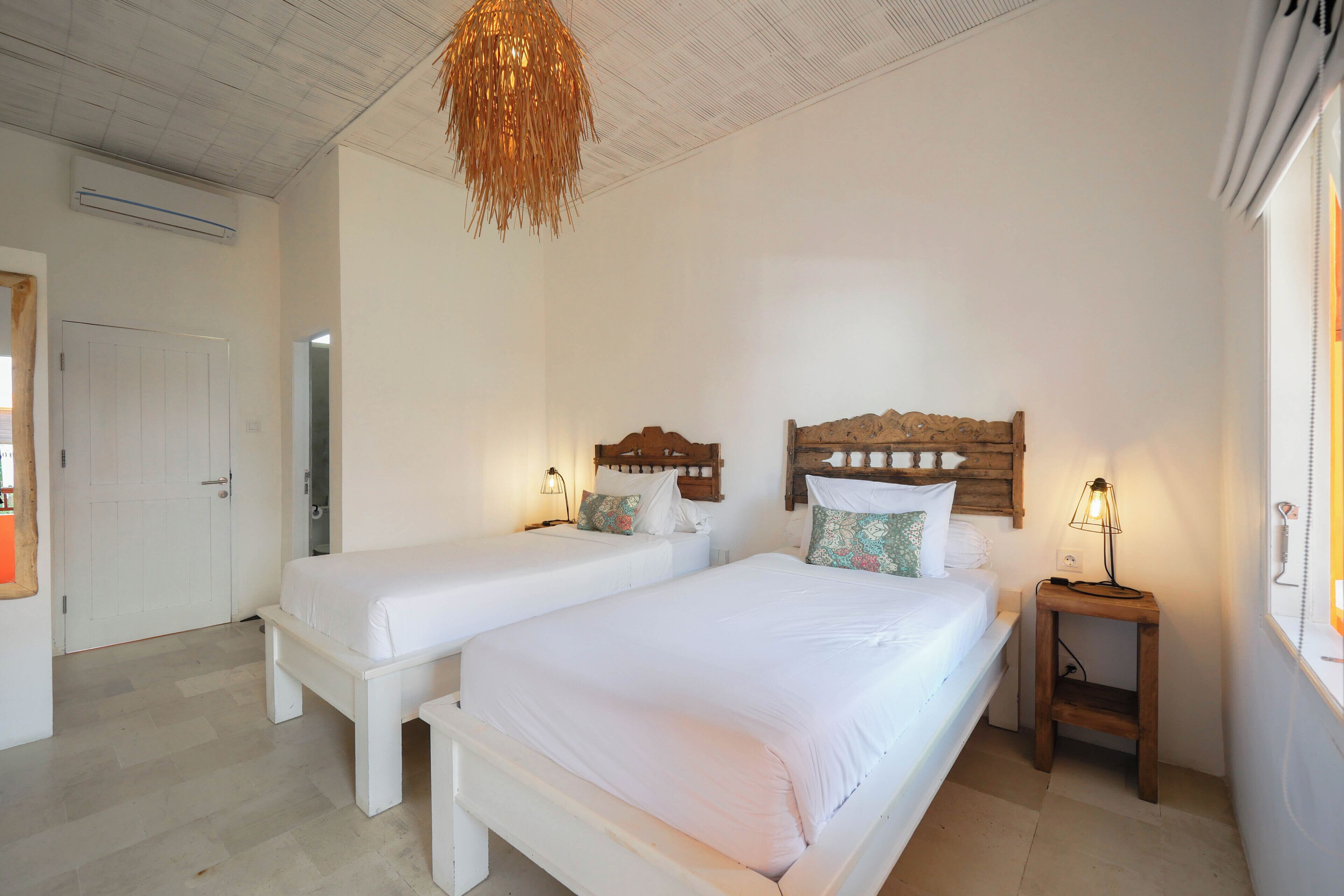 Une chambre avec deux lits simples, une tête de lit en bois, des lampes de chevet et un luminaire suspendu.