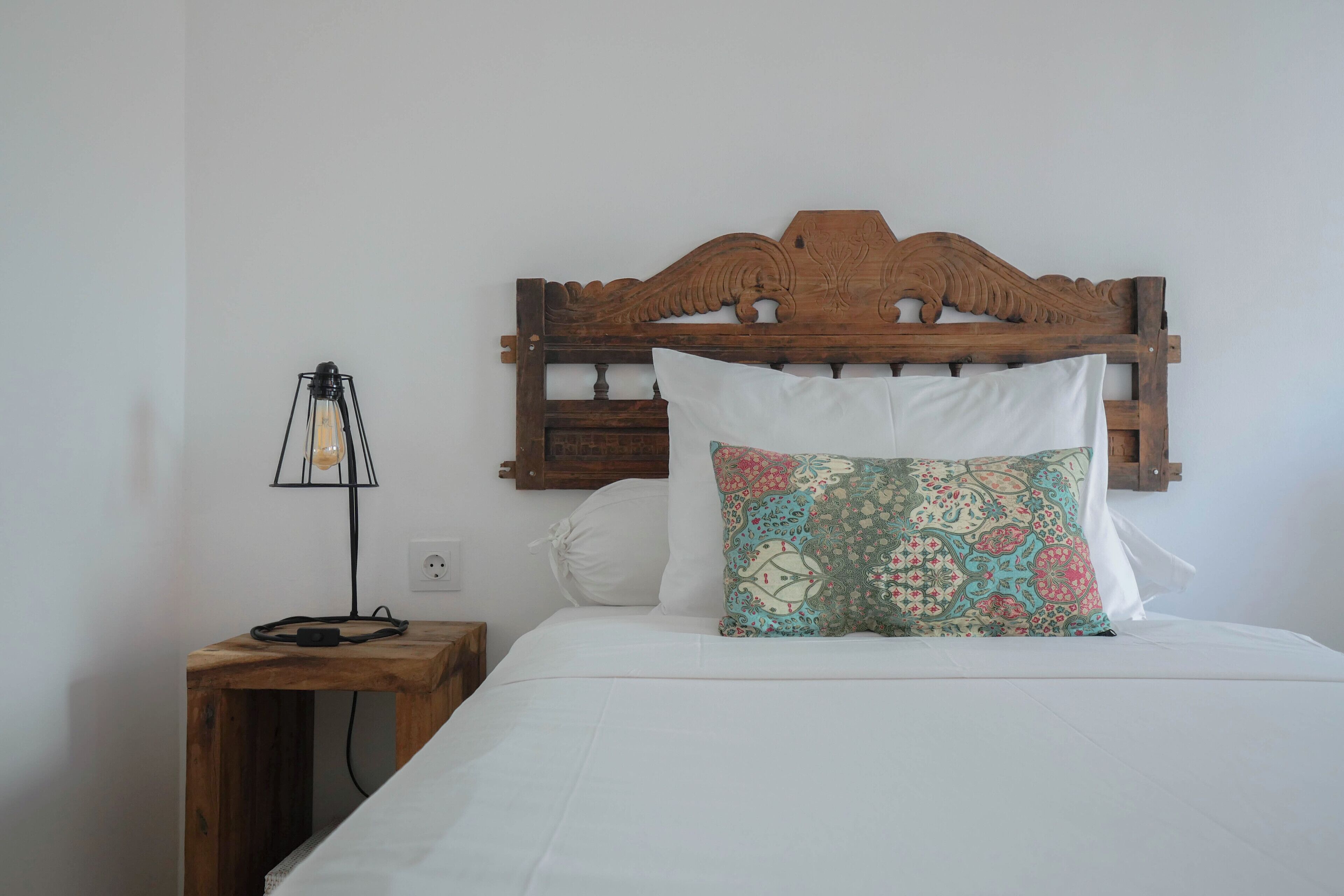 A bed with a wooden headboard, a patterned pillow, a white pillow, and a bedside table with a lamp.