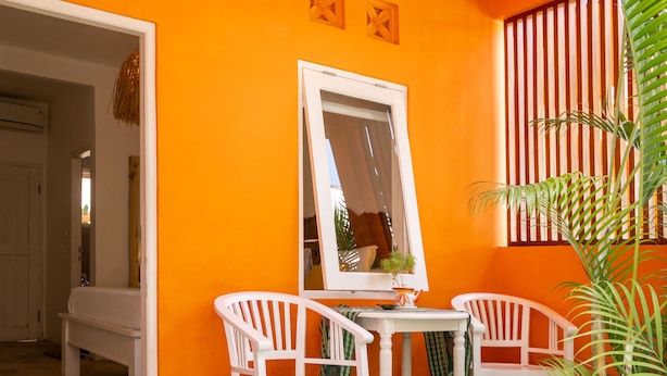 A room with orange walls, white furniture, and a large mirror. - The Room Padang-Padang (Pecatu)