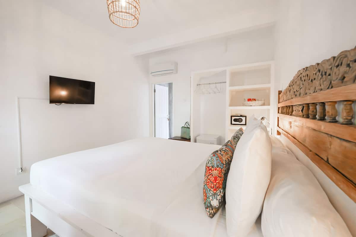 A bedroom with a bed, a TV mounted on the wall, a wooden headboard, and a wardrobe with shelves.