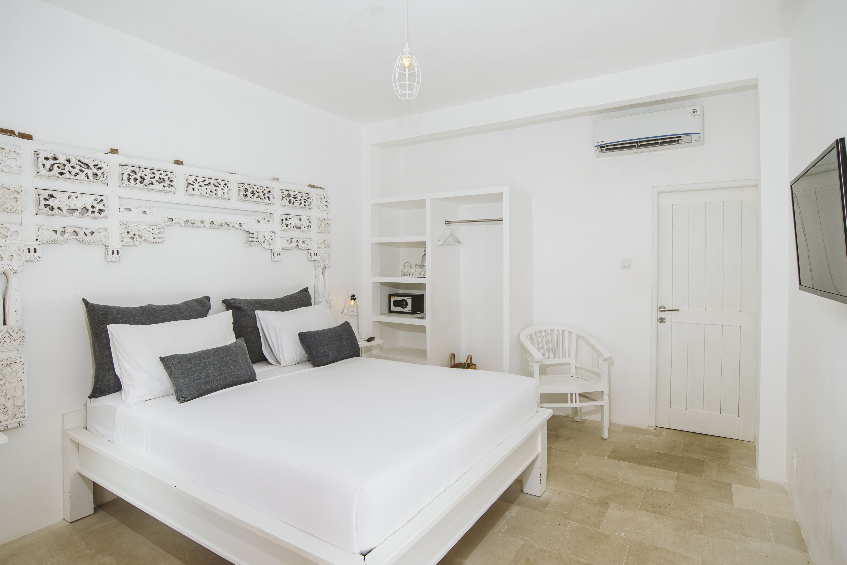 A white bedroom with a bed, a chair, a wardrobe, and a TV.