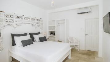 A white bedroom with a bed, a chair, a wardrobe, and a TV.