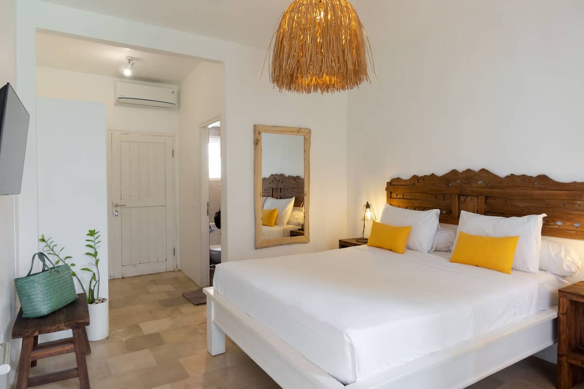 A spacious bedroom with a large bed, a hanging light fixture, a mirror, and a wooden headboard.