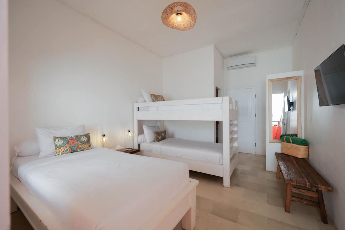 A bedroom with a bunk bed, a single bed, a wooden bench, a wall-mounted TV, and a woven light fixture.