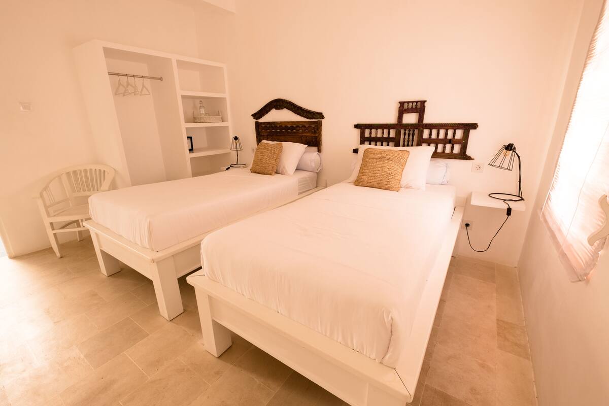 Two single beds with wooden headboards, a white wardrobe, and a bedside table with a lamp.