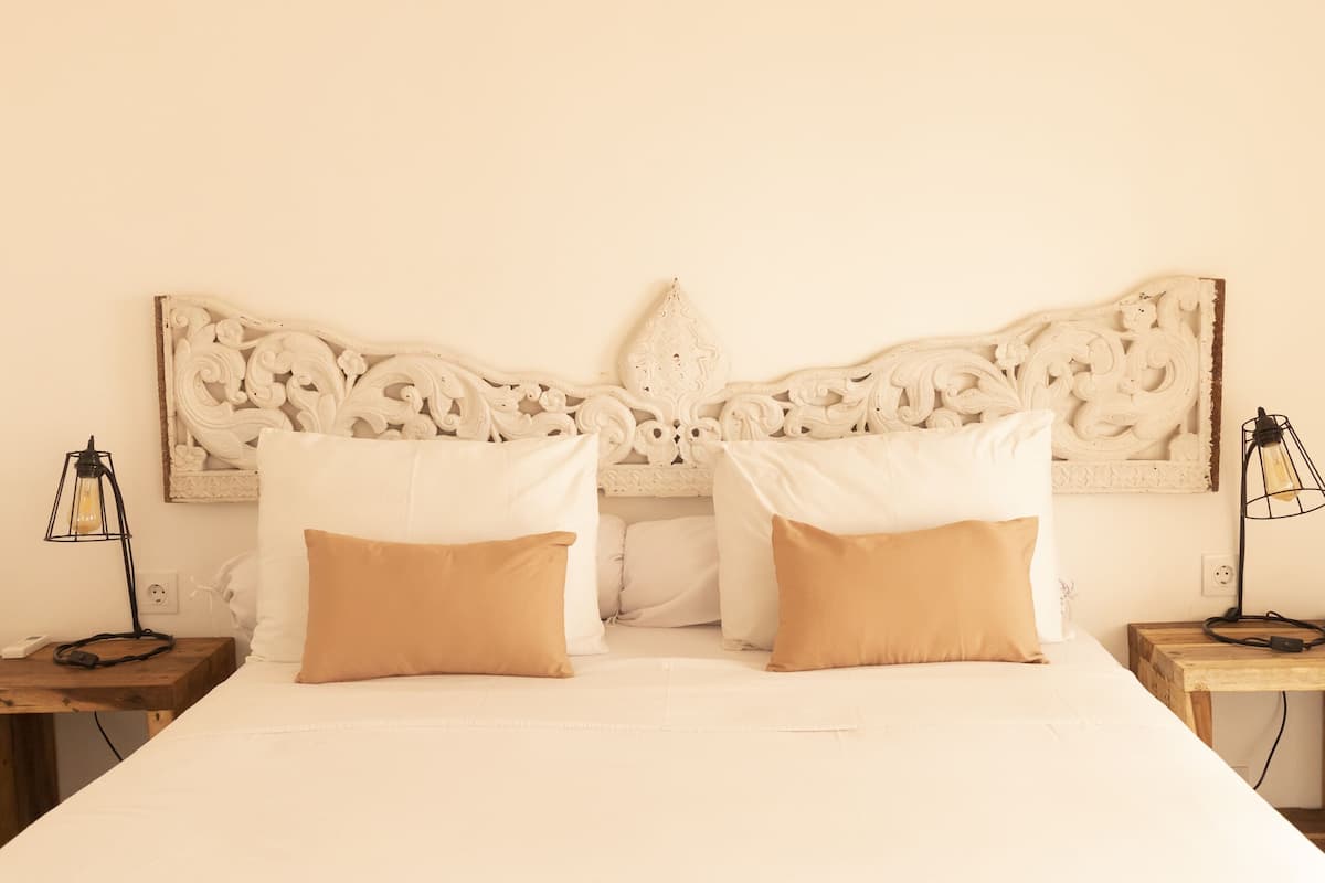A bed with white bedding and two beige pillows, a decorative headboard, and two bedside lamps.