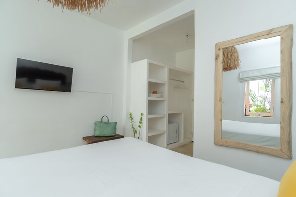 A bedroom with a bed, a TV mounted on the wall, a wardrobe, and a mirror with a view of the outdoors. - The Room Padang-Padang (Pecatu)