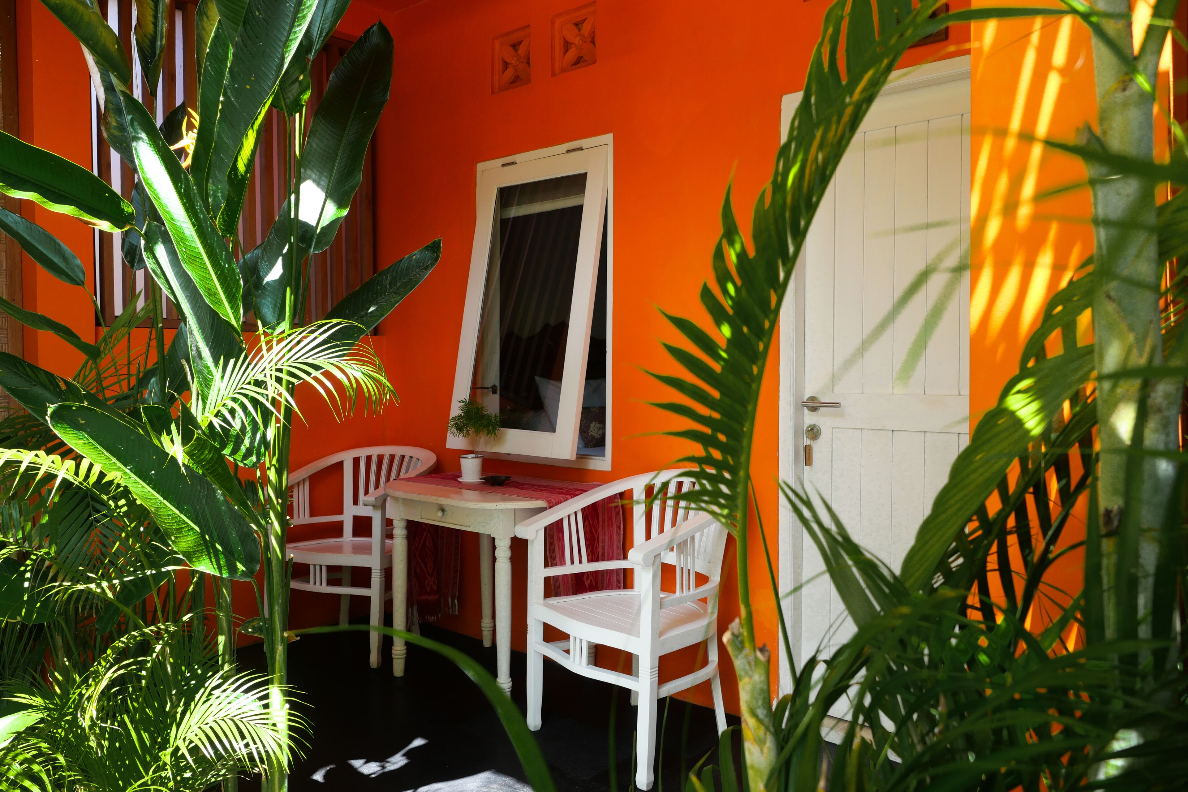 Una habitación con una puerta blanca, una mesa blanca con dos sillas y una planta en maceta.
