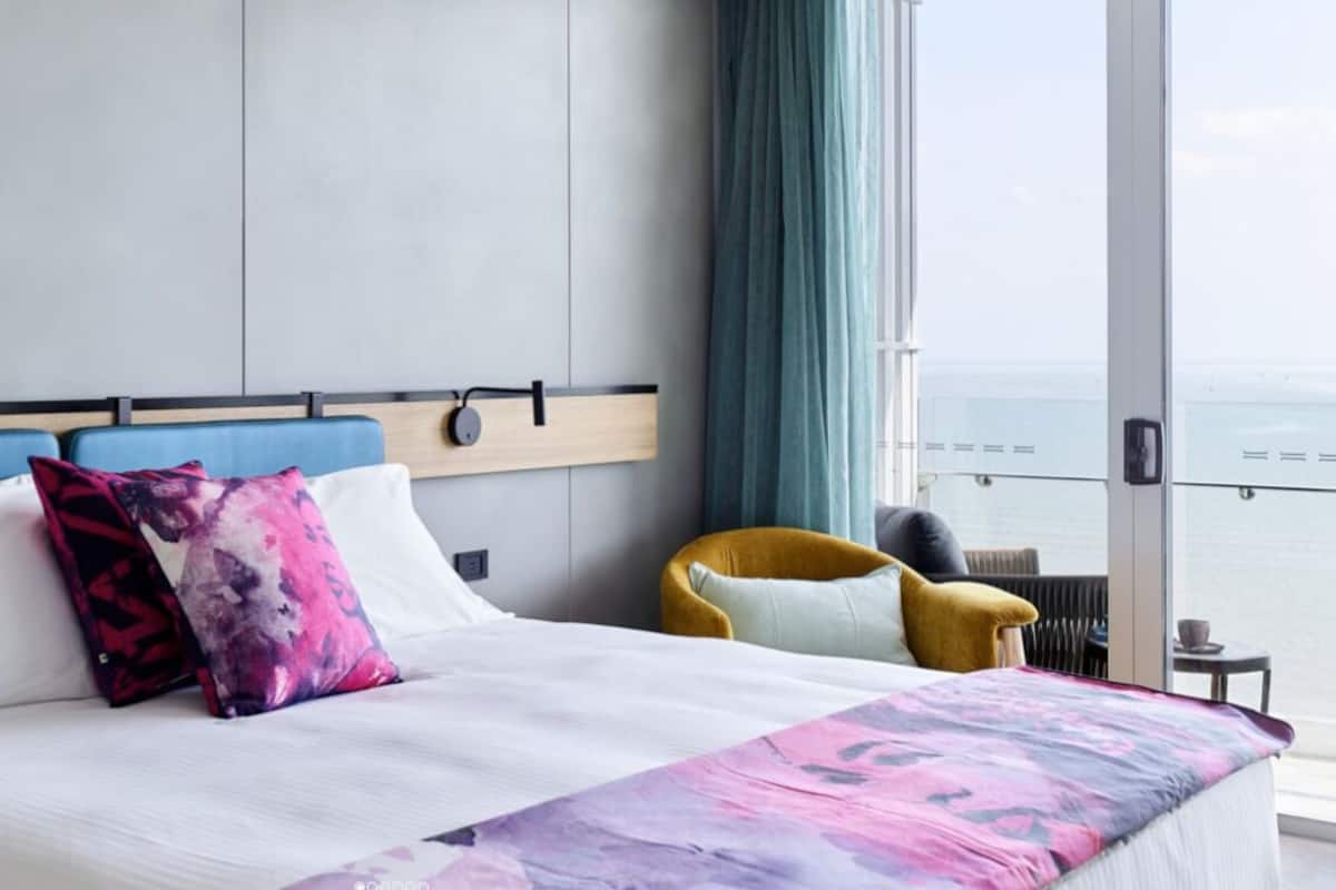 A modern hotel room with a large bed, a view of the sea, and a yellow armchair.