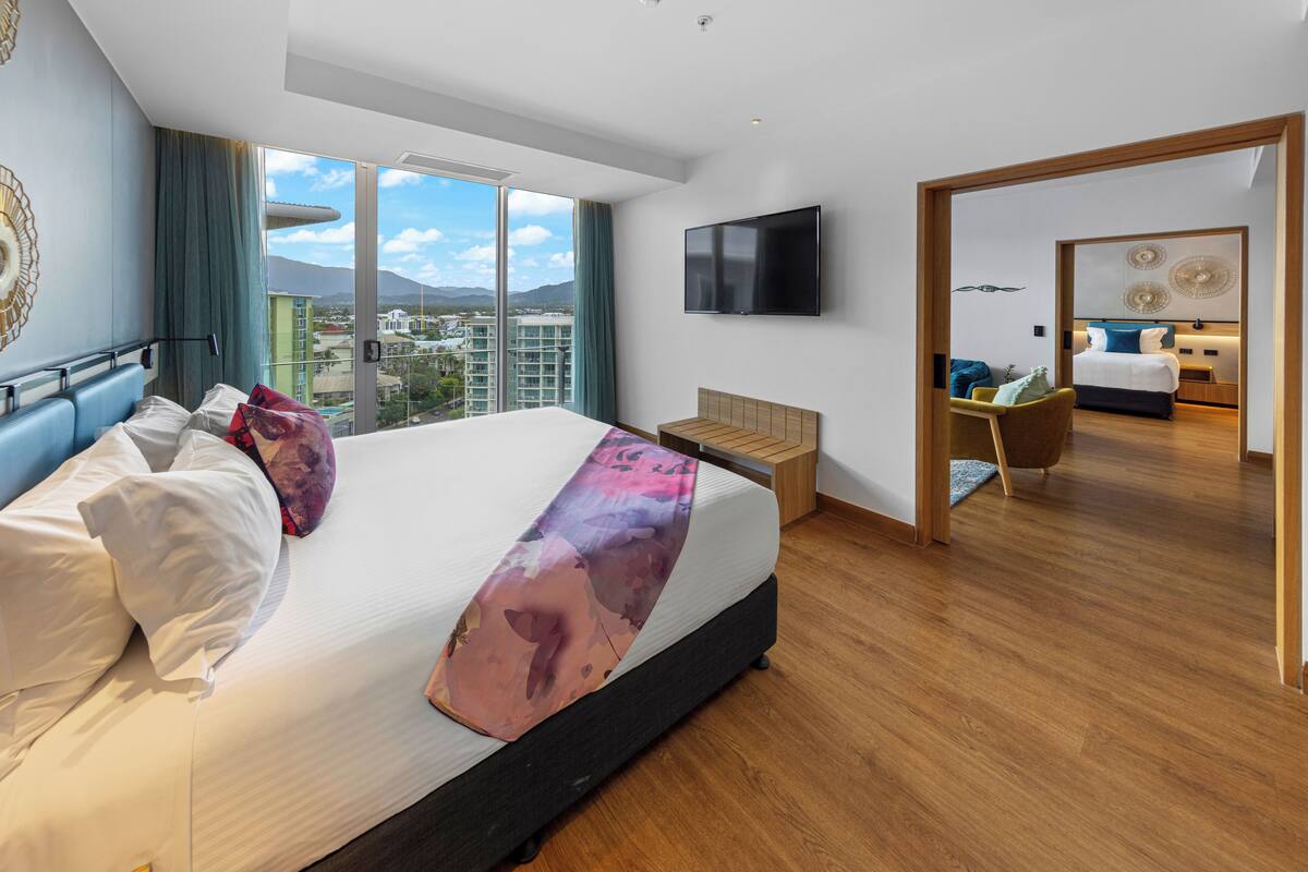 A modern hotel room with a large bed, a TV, and a view of the cityscape.