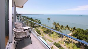 A balcony with wicker chairs and a table, overlooking a coastal view with palm trees and a clear sky. - Crystalbrook Flynn (Cairns)
