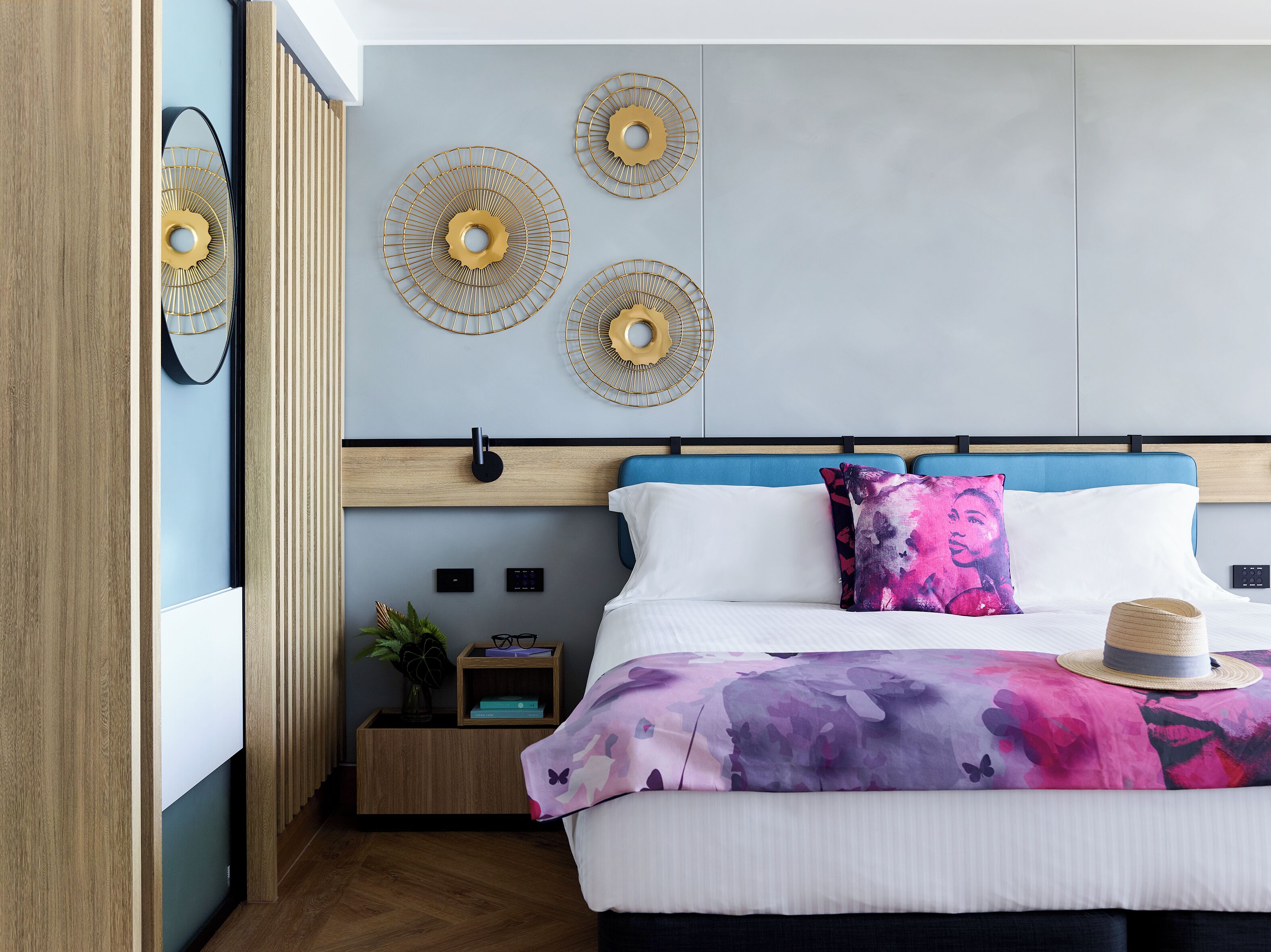 Un dormitorio moderno con una cama, decoración de pared, una mesita de noche con una planta y una mesilla.