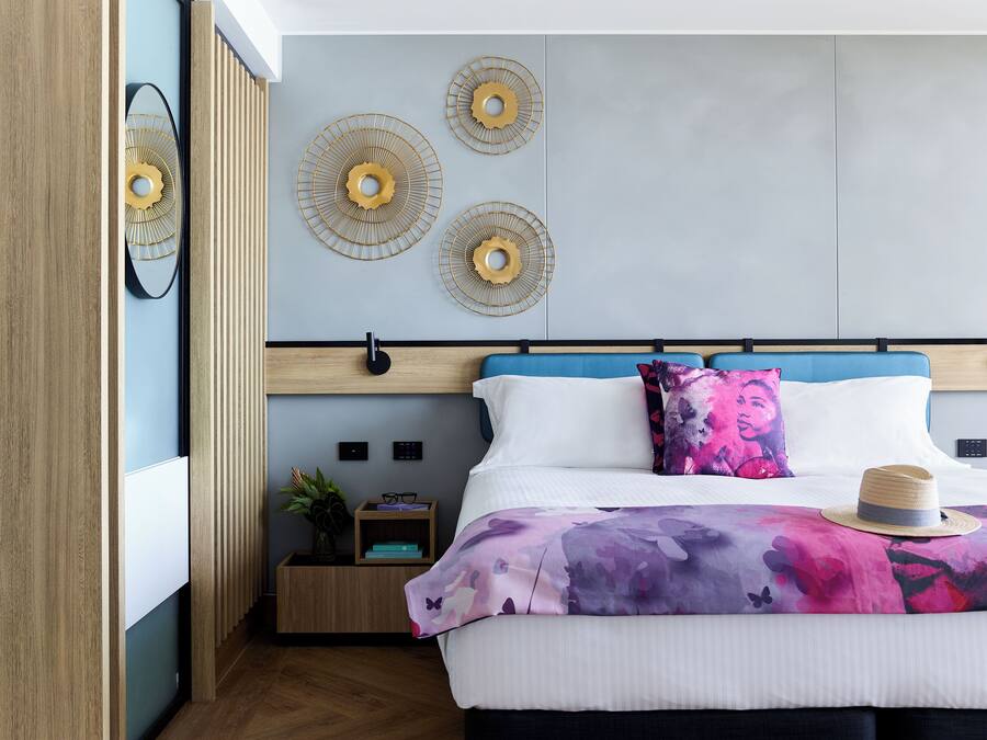 A modern bedroom with a bed, decorative wall art, a bedside table with a plant, and a nightstand.