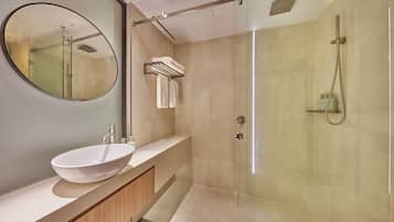 A modern bathroom with a large oval mirror, a white vessel sink, a glass-enclosed shower, and a towel rack.