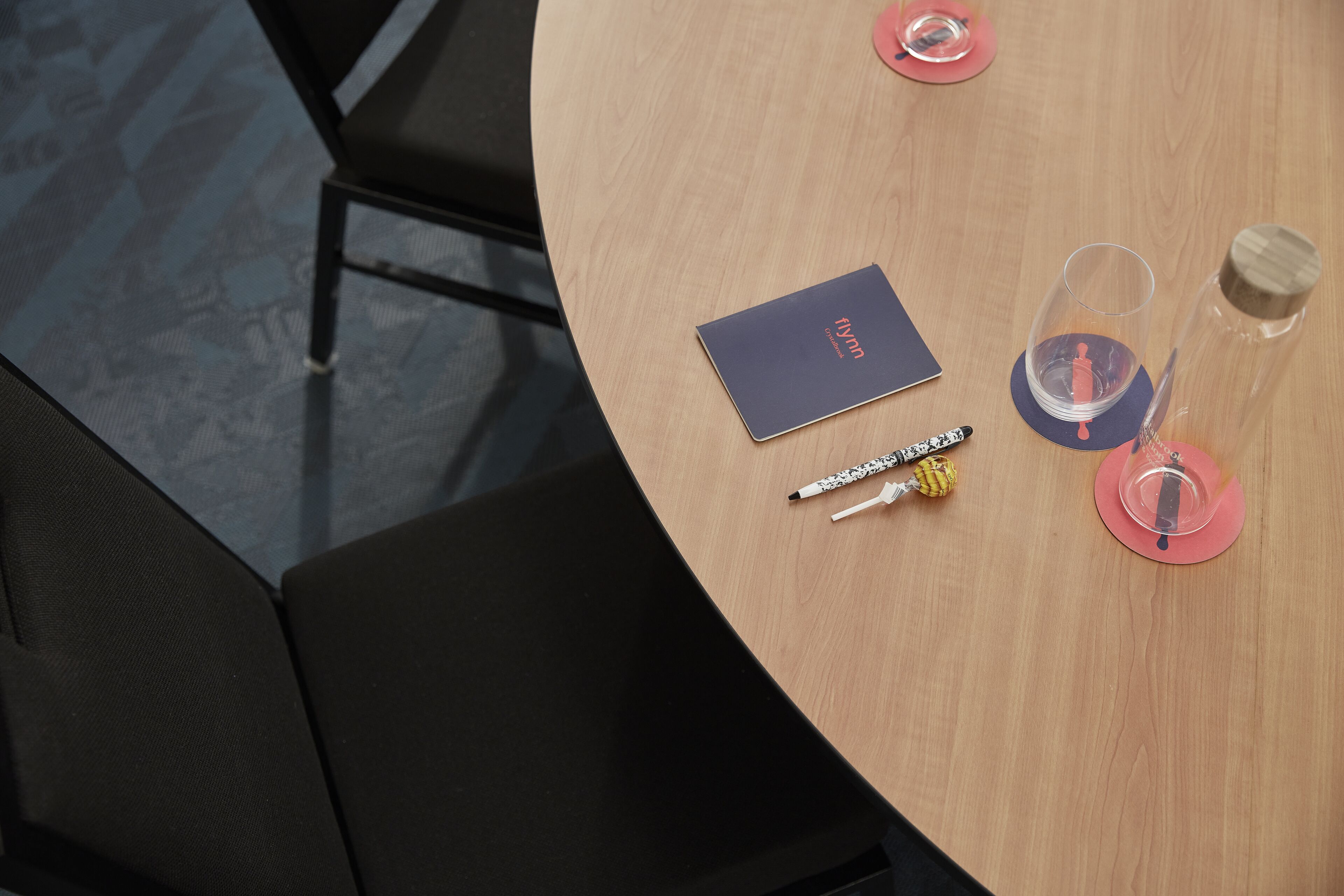 A round wooden table with a notebook, pens, and a glass with a wooden lid.