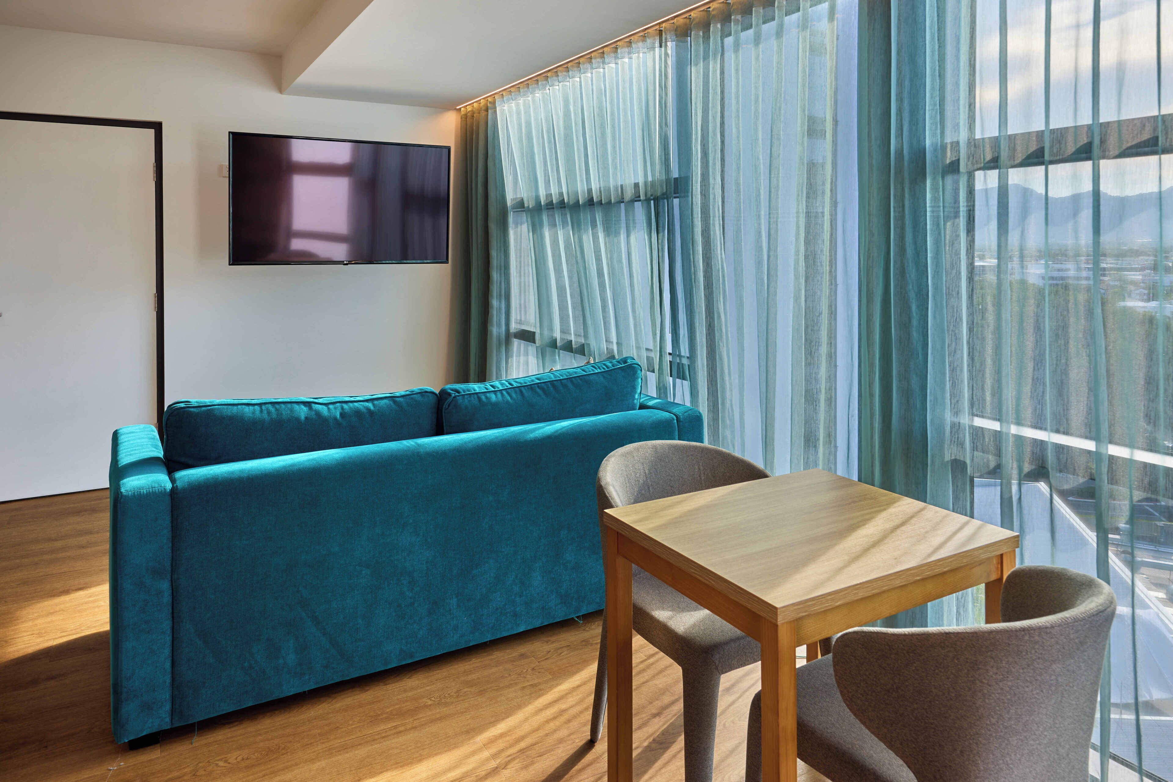A modern living room with a teal sofa, a wooden table, and a TV mounted on the wall.