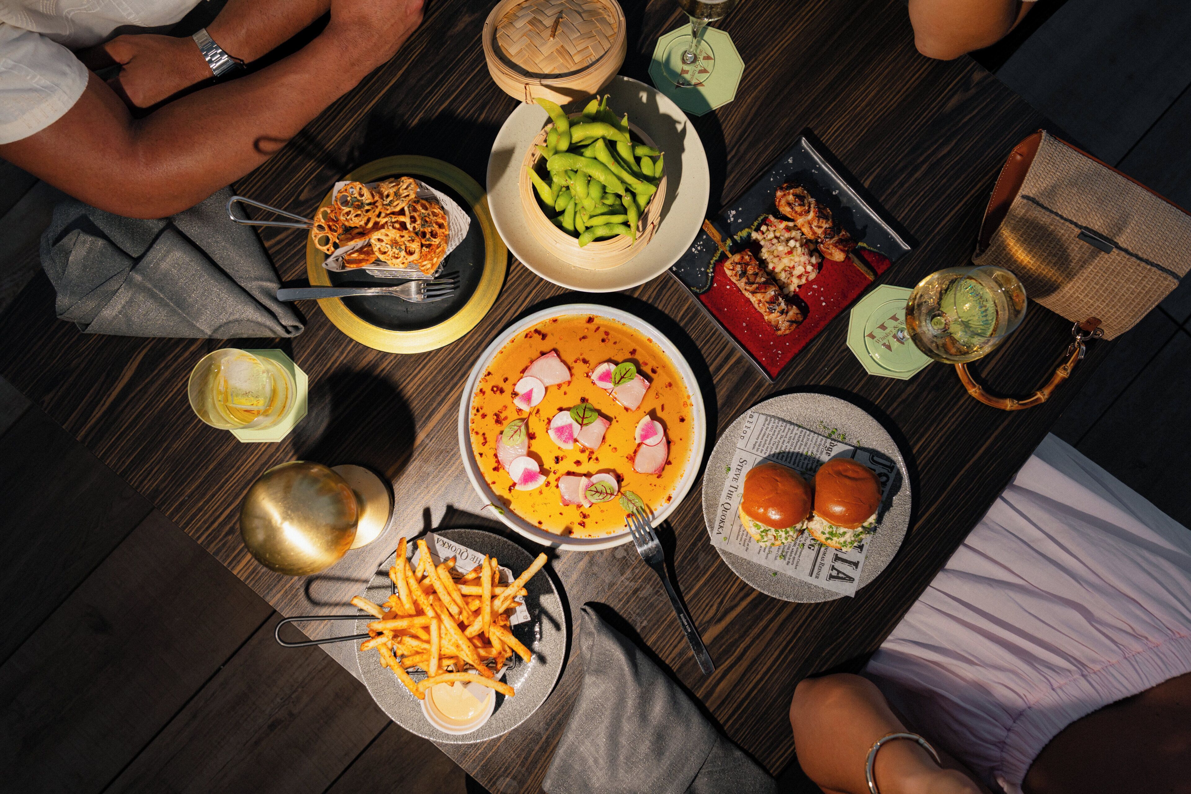 A dining table with various dishes, including a bowl of soup, a plate of fries, and a basket of green vegetables.
