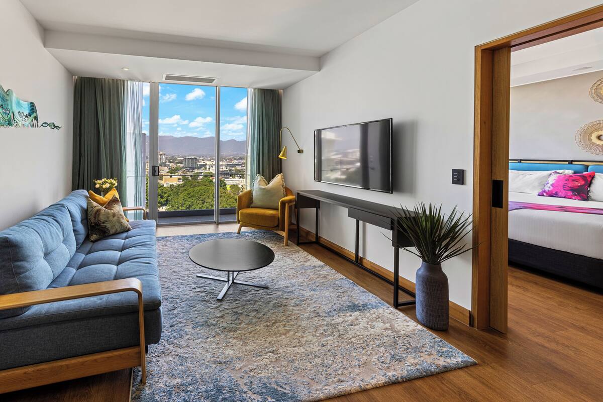 A modern living room with a sofa, a coffee table, a TV, and a view of the city.