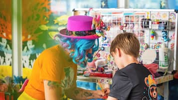 A tattoo artist working on a client's tattoo in a room with colorful murals and a window.